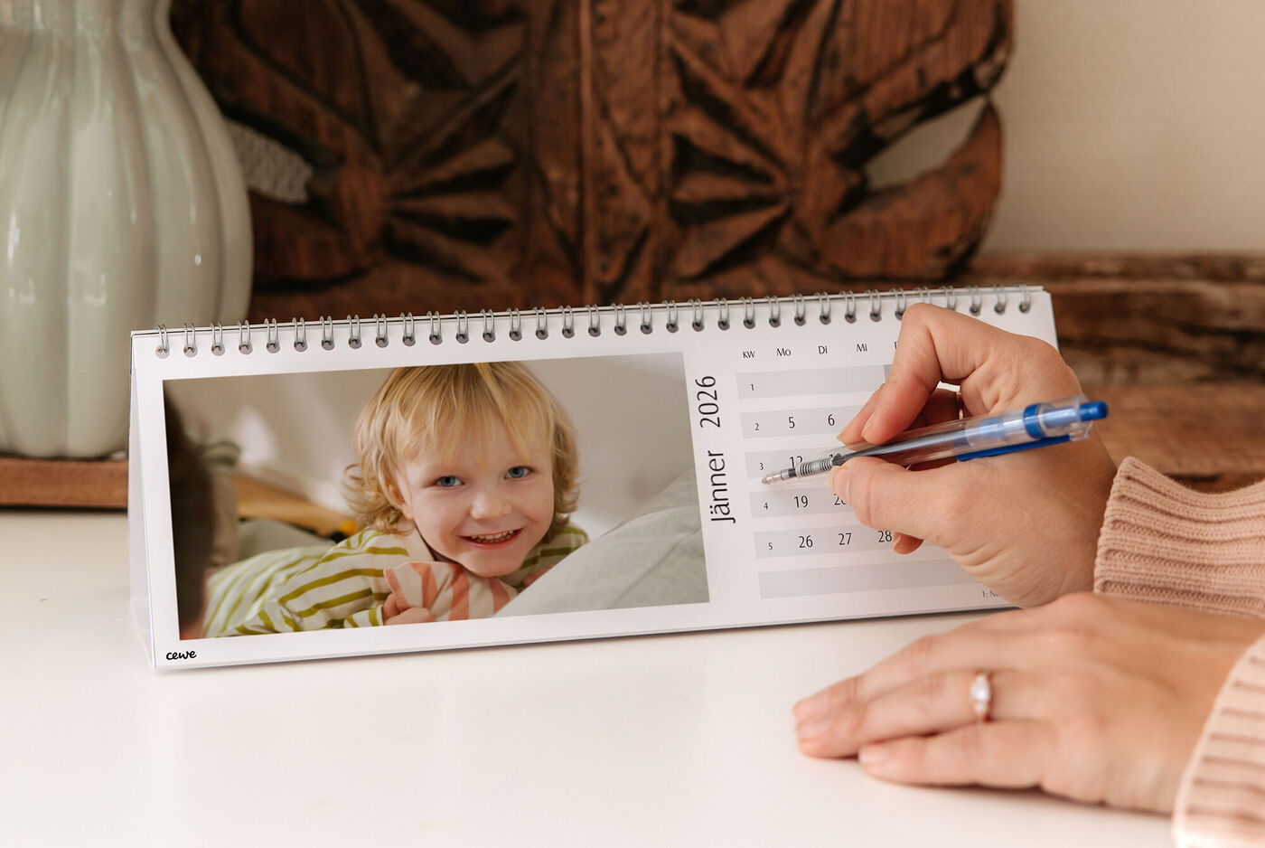 Eine Person schreibt in einen CEWE Fotokalender mit einem Foto an der Seite.