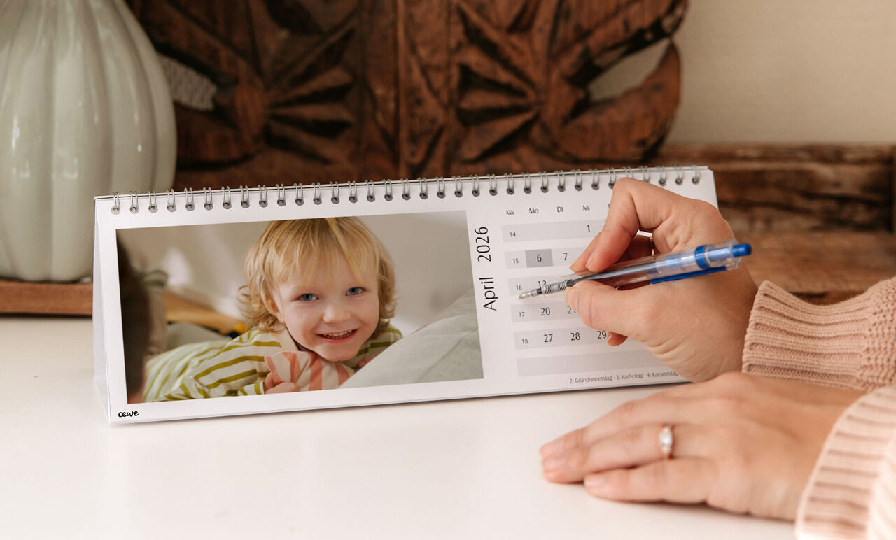 Eine Hand schreibt in einen CEWE Fotokalender für April 2026